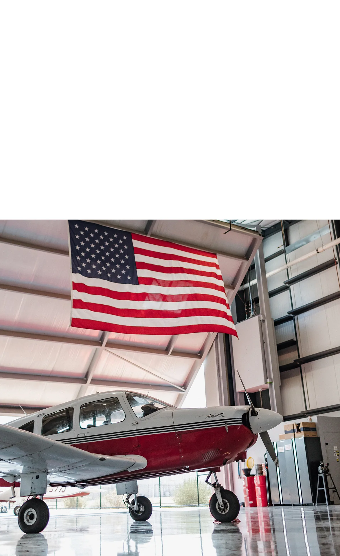Red and white airplane beneath an American flag inside a hangar.