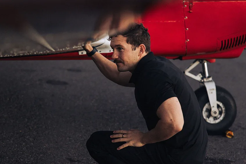 Person crouching beneath the wing of a red and white airplane.