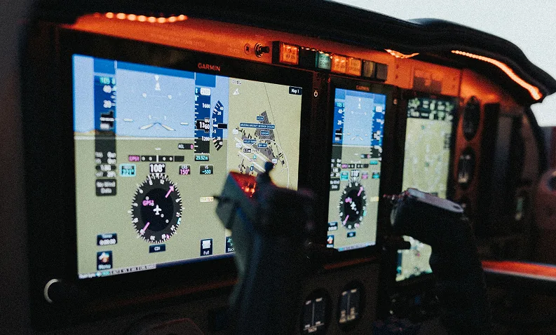 Close view of illuminated digital flight displays and control yokes in a cockpit.