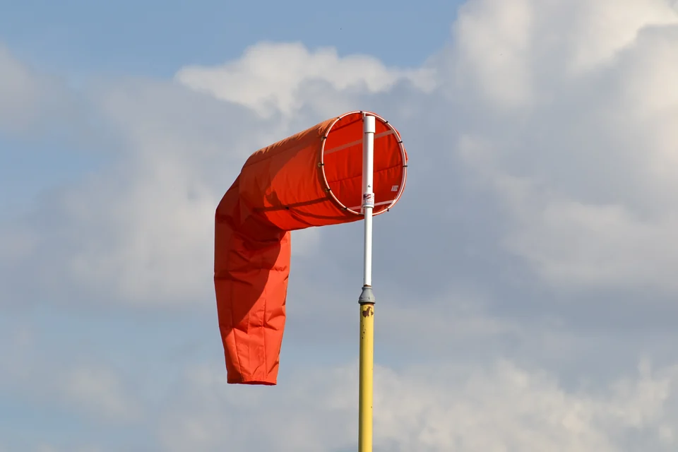 Orange airport windsock with its narrow end hanging down against a blue and cloudy sky.