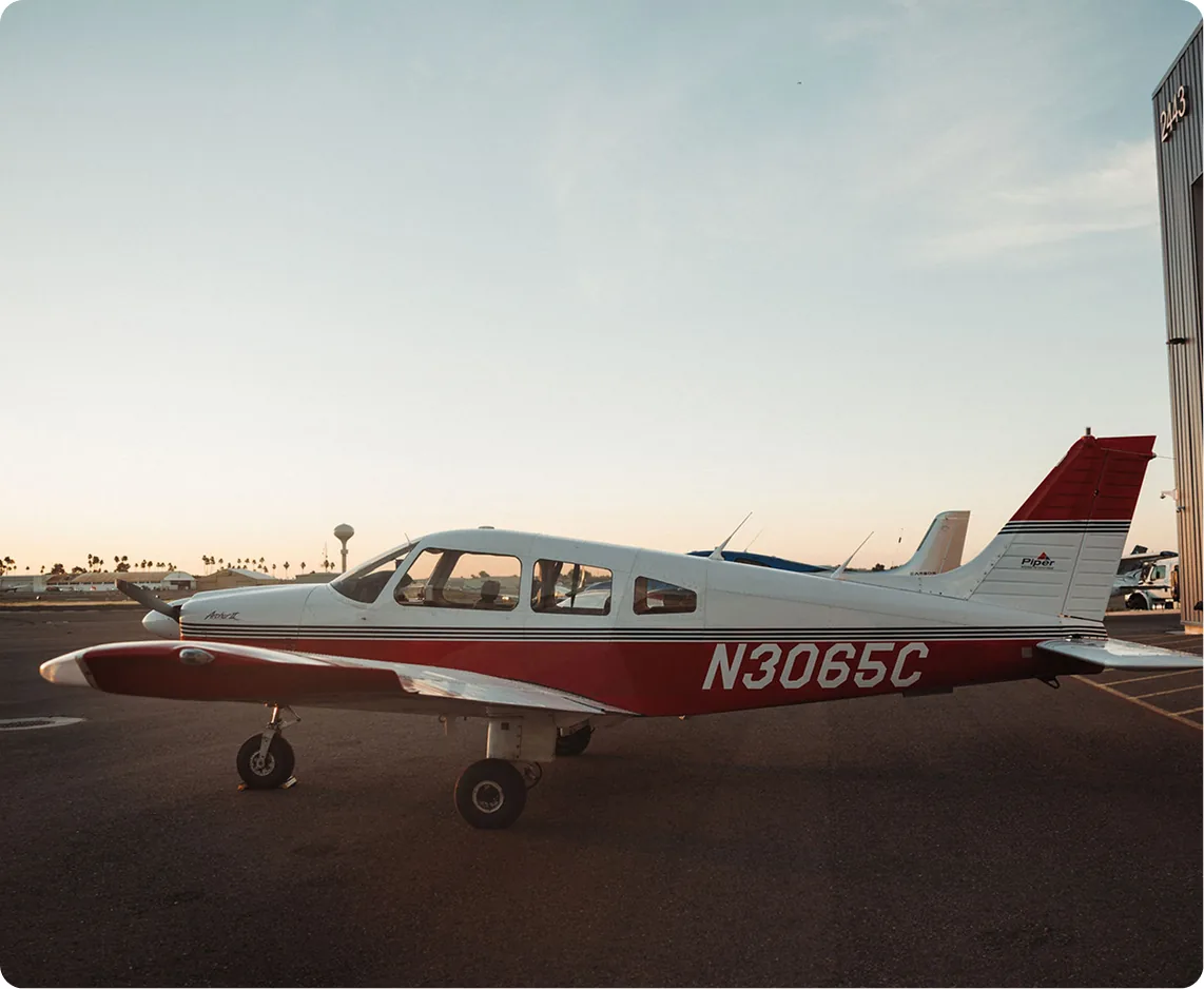 Side view of a red and white airplane parked beside a hangar at sunset.
