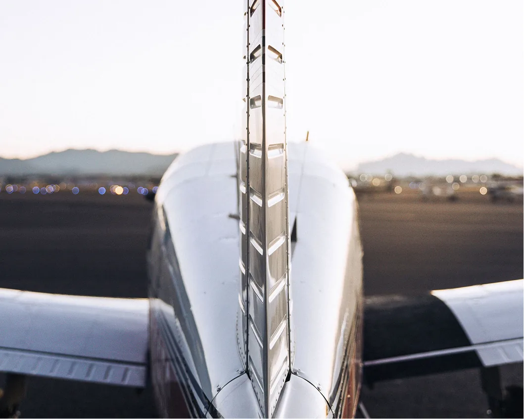 View past an airplane tail toward the airport ramp and distant mountains.